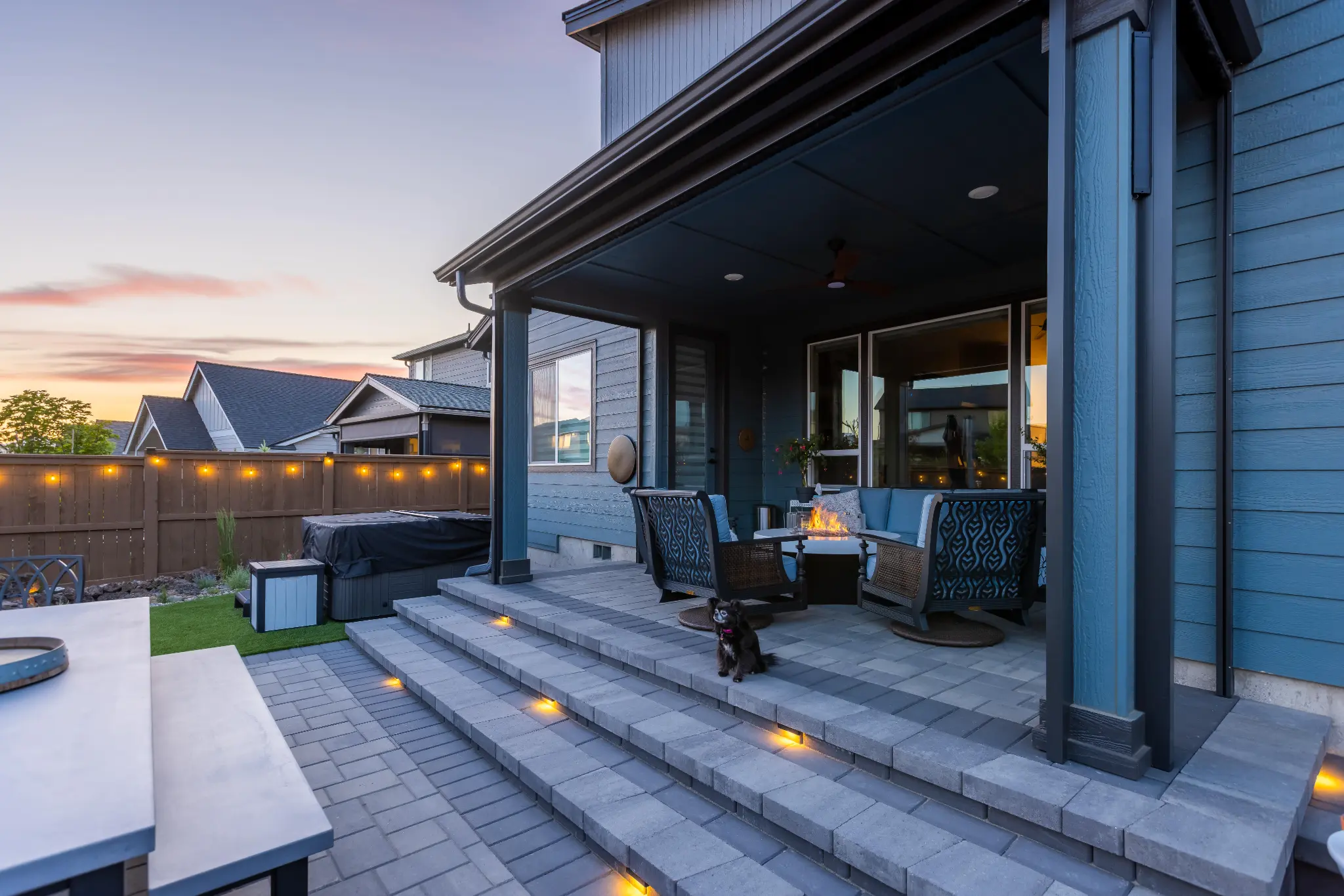 Finished paver patio with curved retaining wall, string lights, and outdoor dining at dusk