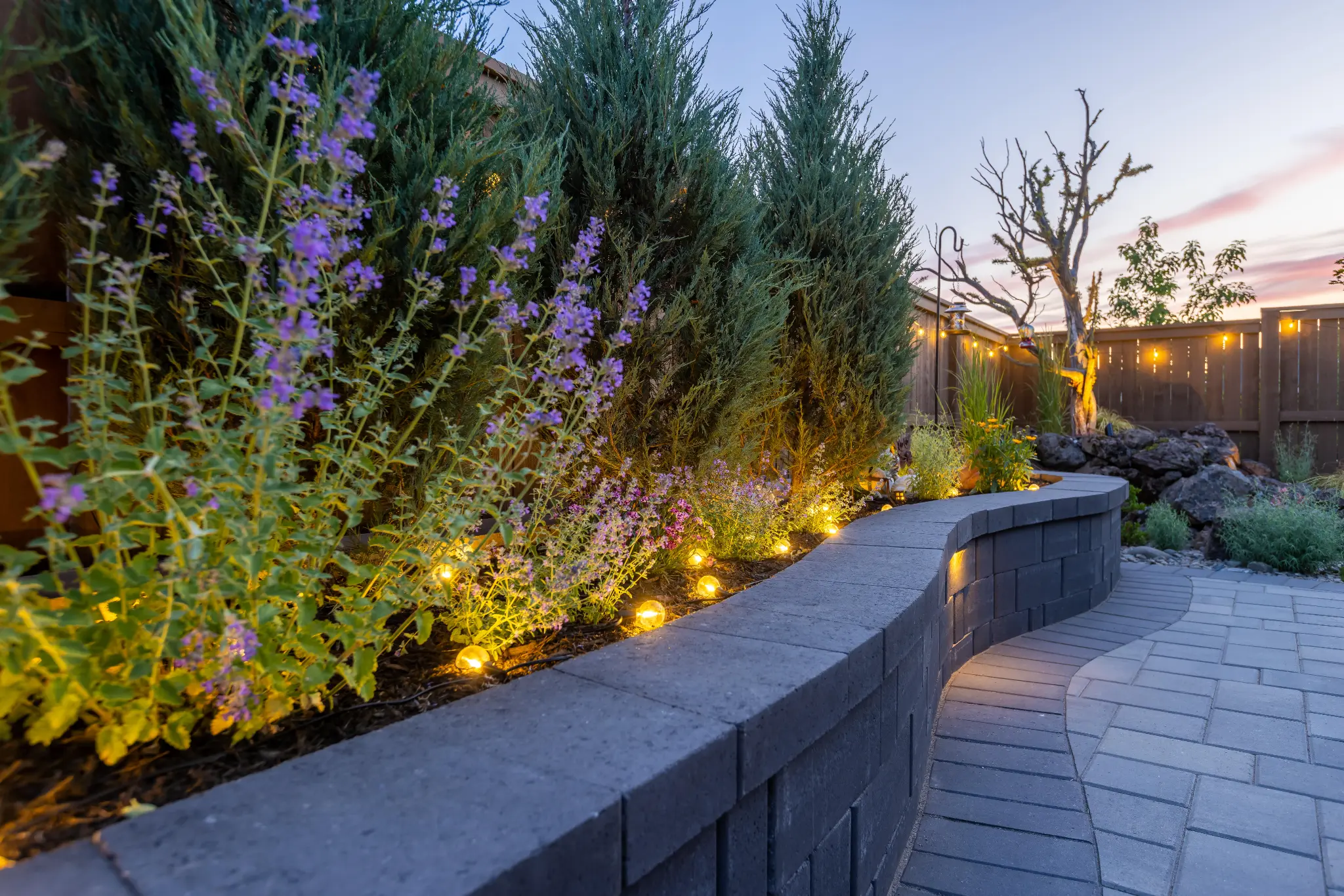 Curved retaining wall with flowering perennials and uplighting at dusk